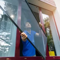 Mężczyzna montuje moskitierę na okno drewniane. Ochrona przed owadami w letnie dni.