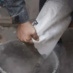 Robotnik wsypuje cement z worka do wiadra. Zastanawiasz się, ile kosztuje tona cementu?