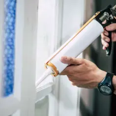 Ręce uszczelniają okno za pomocą pistoletu z silikonem.