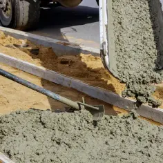 Robotnicy wylewają świeży cement, tworząc chodnik. To właśnie co to jest cement – spoiwo budowlane.