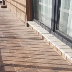 Drewnopodobne płytki na tarasie zewnętrznym, z jasną fugą, tworzą ciepły klimat. Cienie od balustrady dodają uroku.