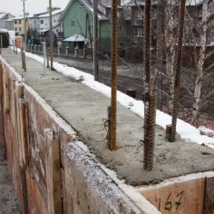 Wylany beton na budowie, a na nim przymrozek. Stalowe pręty wystają z mokrej masy, a wokół leży śnieg.