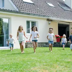 Dzieci biegające po trawniku przed domem z jasną elewacją.