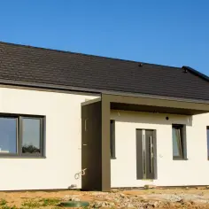 Nowy dom z ciemnym dachem i białymi ścianami, gotowy do odbioru. Brak widocznego ocieplenia.