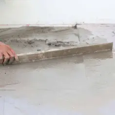 Ręka wyrównuje świeży, gotowy beton na posadzkę za pomocą łaty.