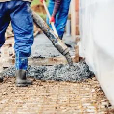 Pracownicy w niebieskich ogrodniczkach i gumowcach wylewają beton na zbrojenie. Zastanawiasz się, ile to jest kubik betonu?