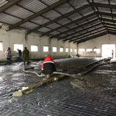 Pracownicy wylewają beton na zbrojenie i folię. Powstaje solidny beton na wylewkę podłogi w hali.
