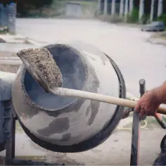 Robotnik miesza łopatą zaprawę cementową gotową w betoniarce.