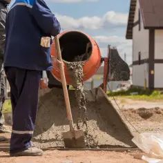 Dwóch budowlańców miesza beton w betoniarce, wylewając go na ziemię.