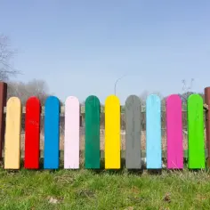 Kolorowy płotek, jakby pomalowany najlepszą farbą do drewna na zewnątrz, wesoło wita wiosnę na zielonej trawie.