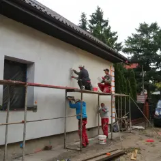 Ekipa budowlana tynkuje elewację domu, pracując na rusztowaniach.