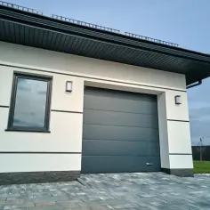 Nowoczesna biała ściana garażu z szarą bramą segmentową. Dowiedz się, ile kosztuje montaż bramy garażowej segmentowej.