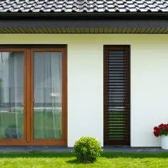Dach antracyt, okna złoty dąb. Biała ściana domu, zieleń trawnika i krzewów, czerwone kwiaty w donicach.