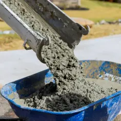 Betoniarka wysypuje świeży beton do taczki. Ten dodatek do cementu jest kluczowy dla budowy.
