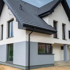 Nowy dom z dwukolorową elewacją, gdzie biały tynk silikonowy na elewacji kontrastuje z szarym cokołem.