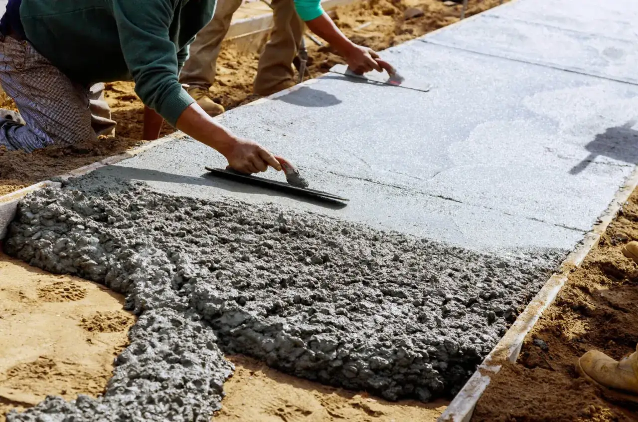 Pracownicy wygładzają świeży beton, przygotowując teren. Wiedza, jak obliczyć metry sześcienne betonu, jest kluczowa dla takich prac.