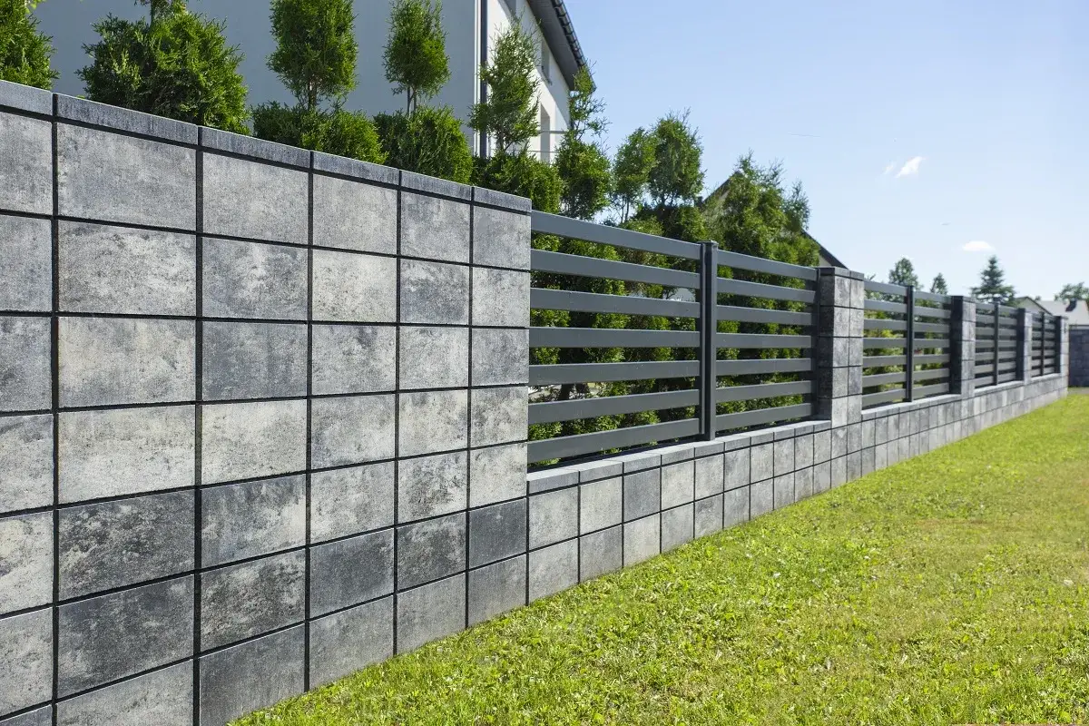 Nowoczesny mur z bloczków betonowych, przechodzący w ażurową, grafitową przęsłową część ogrodzenia.