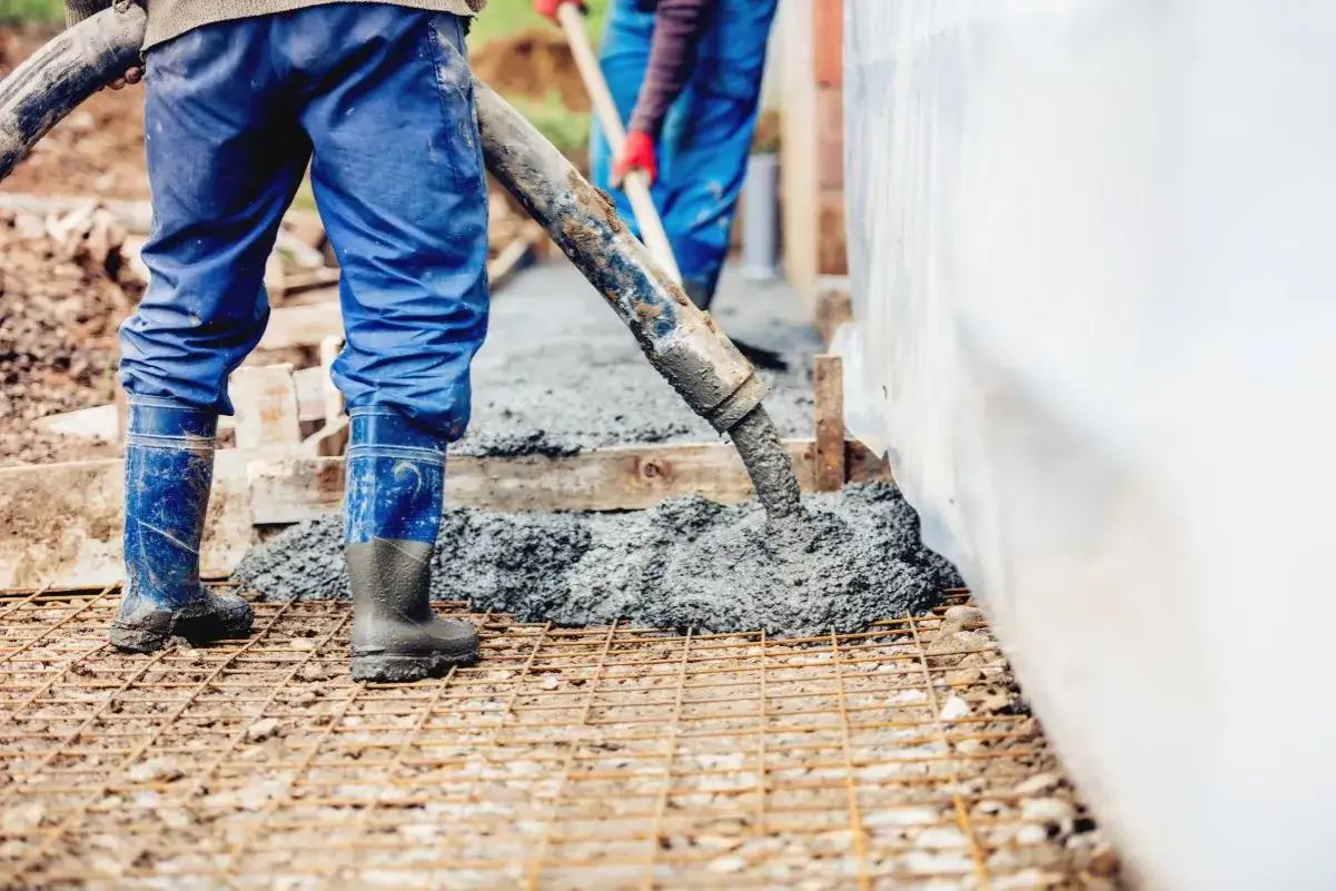 Robotnicy w niebieskich ogrodniczkach i gumowcach wylewają beton. Zastanawiasz się, ile waży kubik betonu?