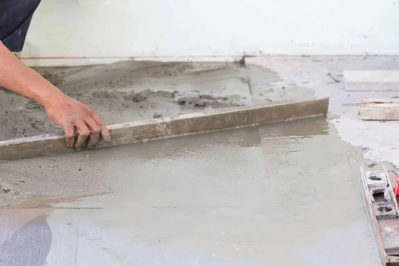 Ręka wyrównuje świeży beton na wylewkę za pomocą łaty.