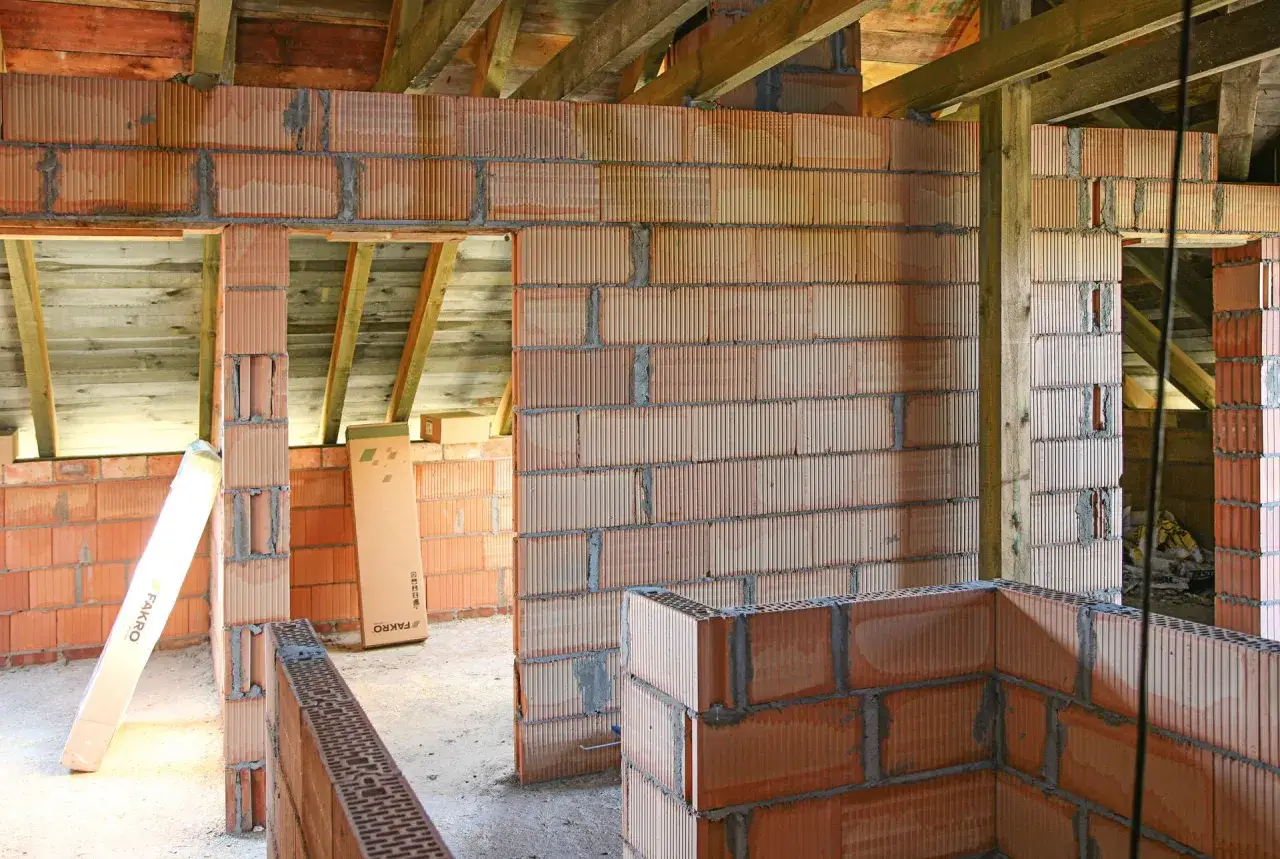 Budowa domu w toku. Ściany z pustaków ceramicznych, widoczna zaprawa do murowania i drewniana konstrukcja dachu.